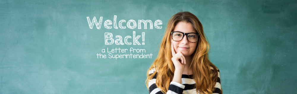 A preteen girl standing in front of a green chalkboard with the text "Welcome Back! a Letter from the Superintendent"