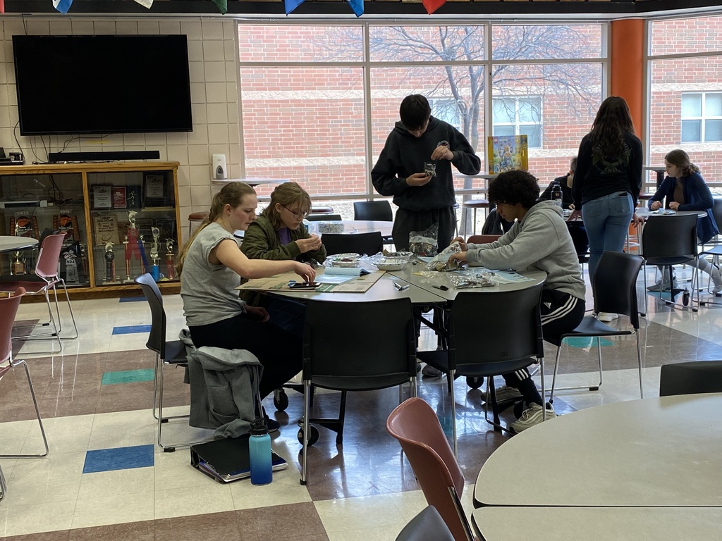 High School Student gathered around a round table in front of windows.